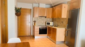 Una cocina compacta con armarios de madera, un refrigerador de acero inoxidable, un microondas y un lavamanos.