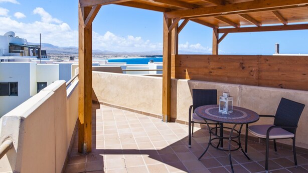 Un balcón con pérgola de madera, con una mesa redonda y dos sillas, con vista a un paisaje costero.