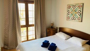 Habitación de hotel con cama, dos almohadas, mesita de noche con lámpara y ventana con cortinas.