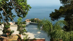 A terrace with a view of the sea, surrounded by greenery and a building with a tiled roof. - Charming  elegantly  apt in villa near the center but in a very quite area (taormina)