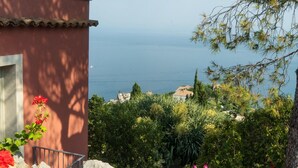 A coastal view with a building, lush greenery, and a clear sky. - Charming  elegantly  apt in villa near the center but in a very quite area (taormina)