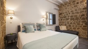 Une chambre avec un grand lit, deux lampes de chevet, un mur en pierre et une fenêtre.