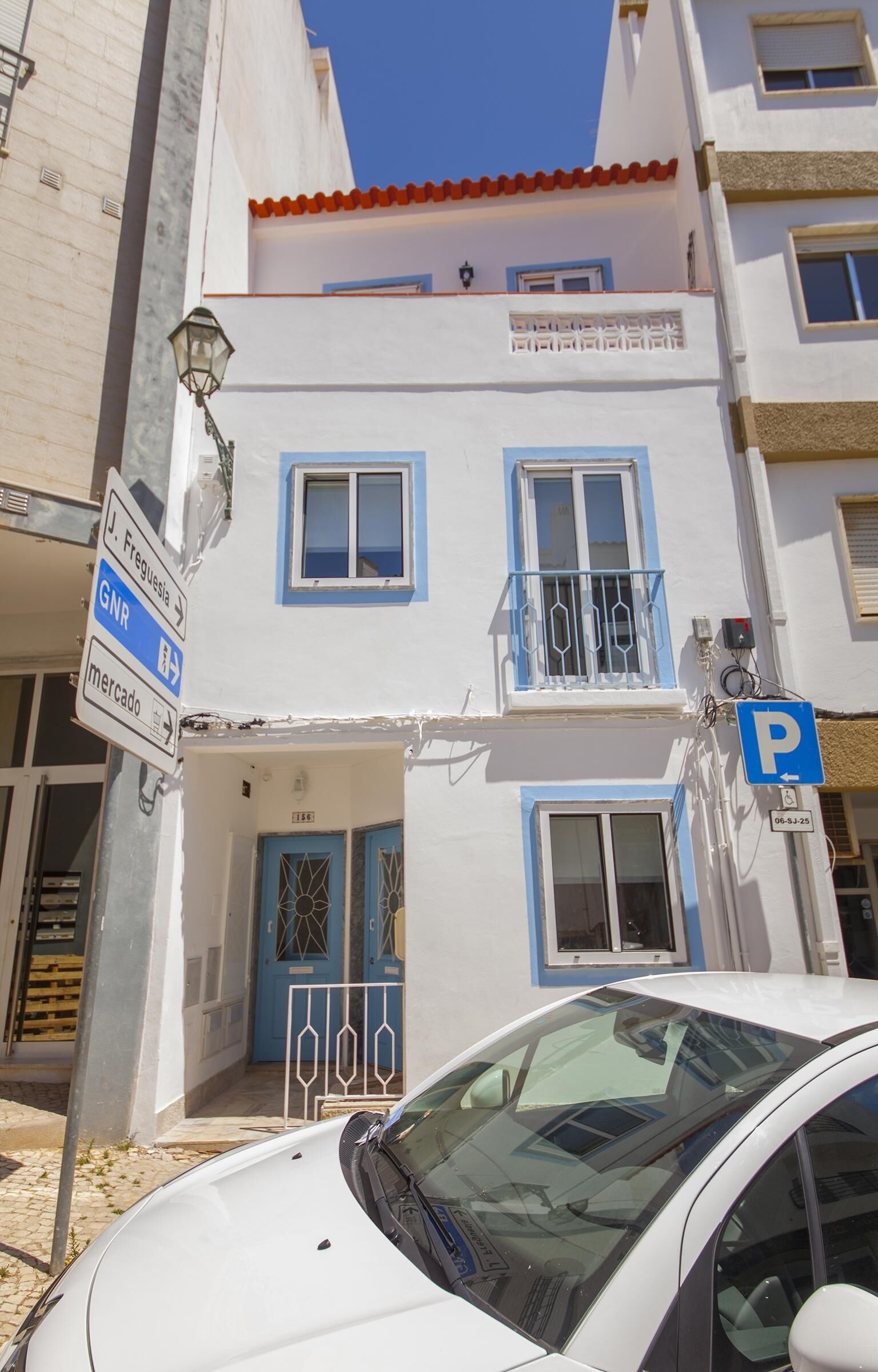A white building with blue accents, a parking sign, and a car parked in front.