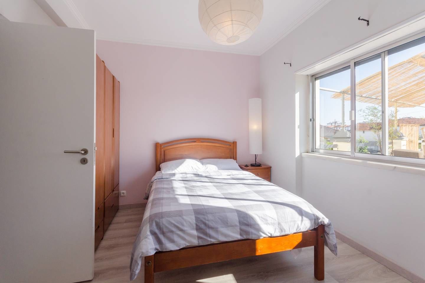 A bedroom with a wooden bed, a nightstand, a lamp, and a window with a view of buildings.