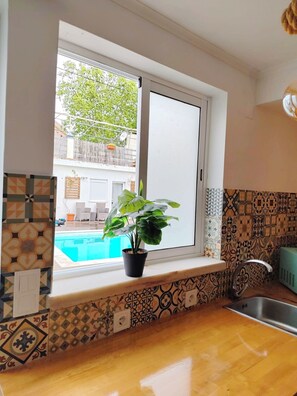 Una cocina con ventana, una planta en maceta, un lavamanos y azulejos con diseño.