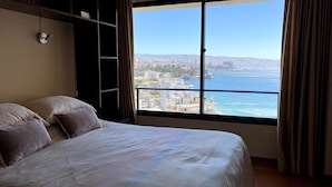 Een slaapkamer met een groot raam, met uitzicht op de stad en de oceaan.
