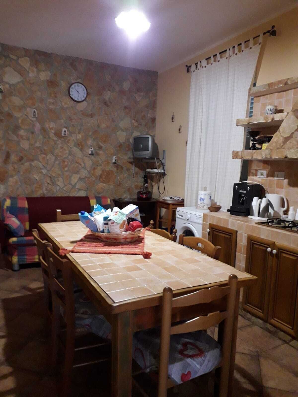 A dining area with a stone wall, a clock, a television, and a kitchen area with a washing machine and a coffee maker.