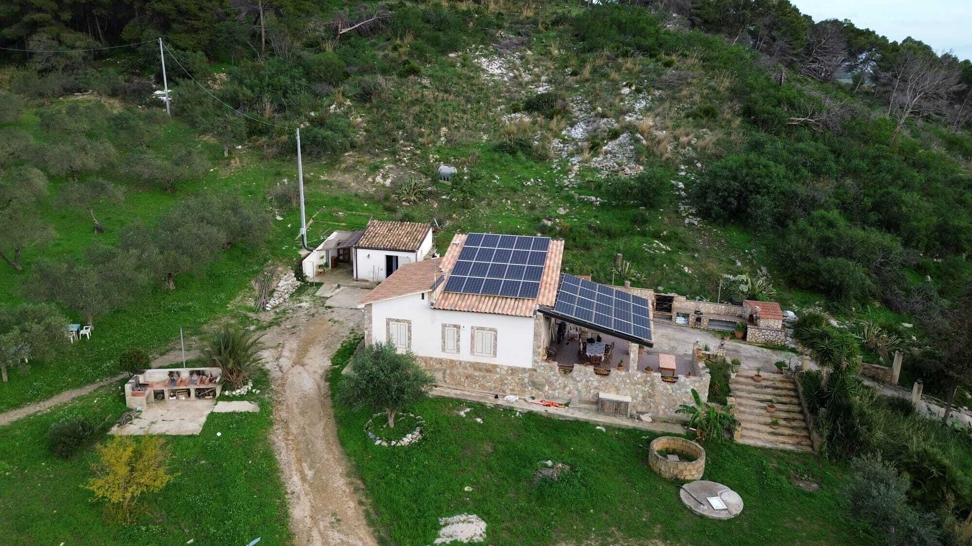 A rural property with a house featuring a solar panel roof, a stone pathway, and a small garden.