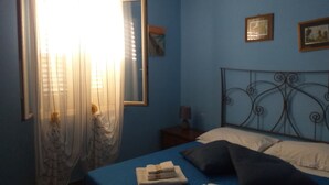 Un dormitorio con cama, mesita de noche, espejo y ventana con cortinas.