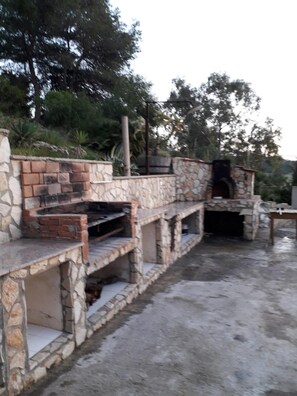 Un espace cuisine extérieur en pierre, doté d’une cheminée en briques et d’un banc en pierre.