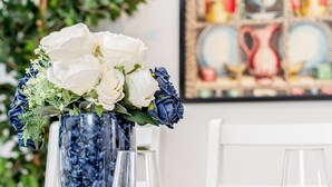 A dining table set with white plates, bowls, and cutlery, a vase with white and blue flowers, and a framed picture in the background. - Luxury 4bed home 2min from High Street Ken/Olympia (London)