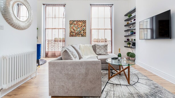 A modern living room with a sofa, a glass coffee table, and a TV mounted on the wall. - Luxury 4bed home 2min from High Street Ken/Olympia (London)