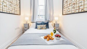 A neatly arranged bedroom with a bed, bedside tables, a window with curtains, and artwork on the walls. - Luxury 4bed home 2min from High Street Ken/Olympia (London)