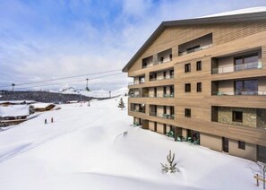 A multi-story hotel with a wooden facade, balconies, and a view of a snowy mountain landscape.