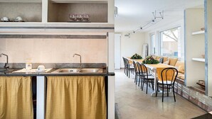 Une cuisine moderne dotée d’un îlot central, d’un coin repas avec une longue table et des chaises, et offrant une vue sur l’extérieur grâce à de grandes fenêtres.