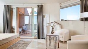 Une chambre d’hôtel moderne avec un balcon, un lit, un canapé et une petite table agrémentée d’un élément décoratif.