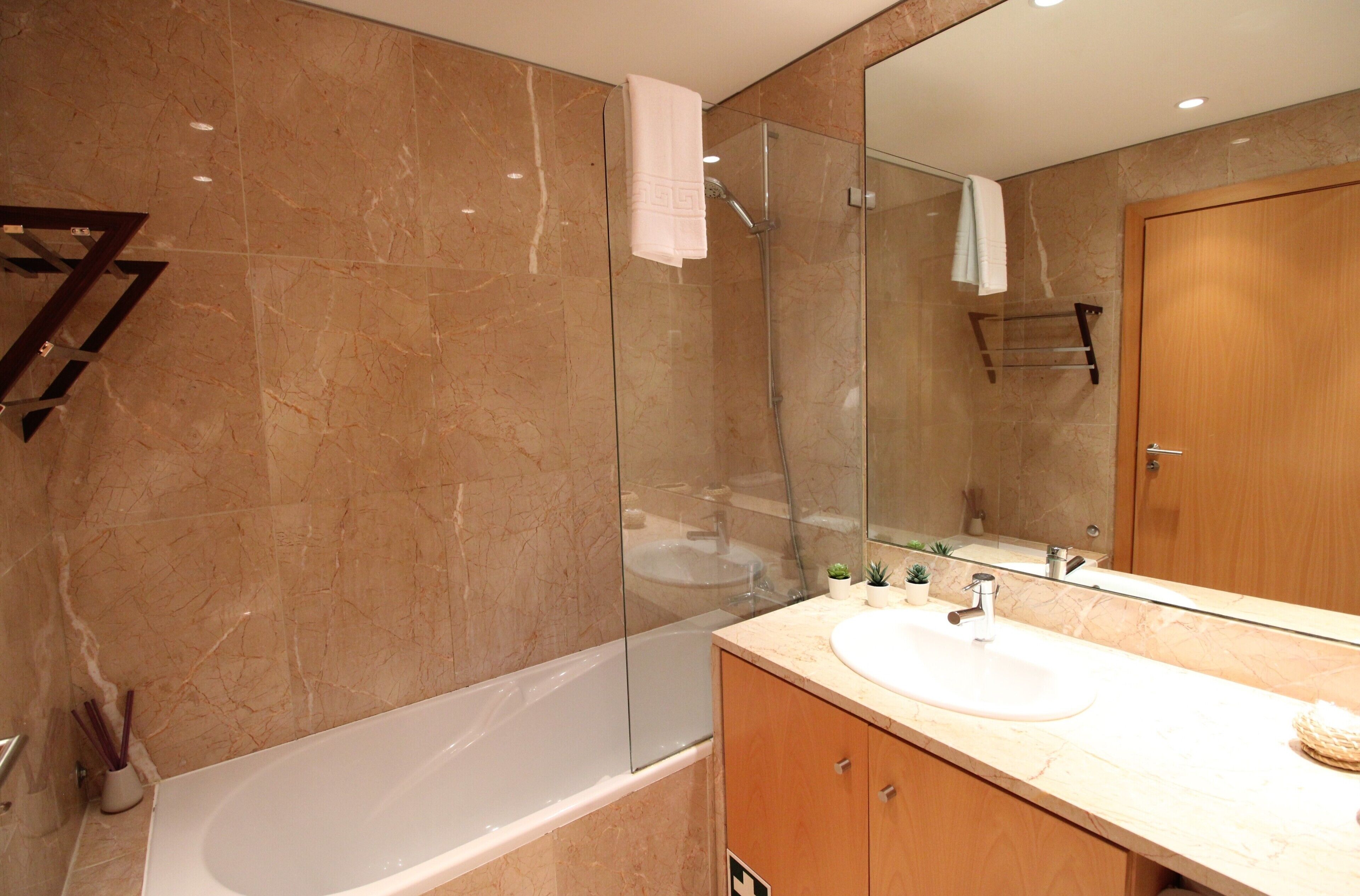 A modern bathroom with a marble wall, a glass-enclosed shower, a wooden vanity, and a large mirror.