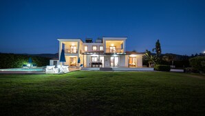 Una casa moderna de dos pisos con un patio delantero bien iluminado, piscina y jardín ajardinado.