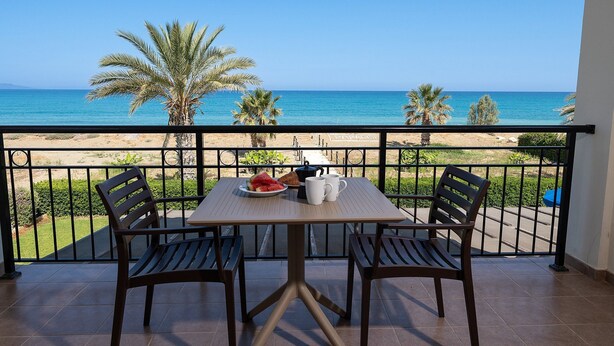 Un balcón con una mesa y sillas, con vista a una playa con palmeras y el mar.