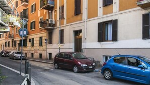 Una calle con coches estacionados, edificios con balcones y un cielo despejado.