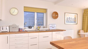 A modern kitchen with white cabinetry, a wooden countertop, a built-in oven, a sink, and a window with blinds. - Stunning beach cottage for the perfect British family holiday with 3 bedrooms (Pevensey Bay)