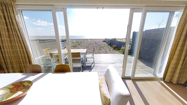 A room with a sliding glass door leading to a deck with a view of the beach and ocean. - Stunning beach cottage for the perfect British family holiday with 3 bedrooms (Pevensey Bay)