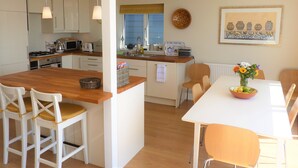 A modern kitchen with white cabinets, a wooden island, and a dining area with a white table and chairs. - Stunning beach cottage for the perfect British family holiday with 3 bedrooms (Pevensey Bay)