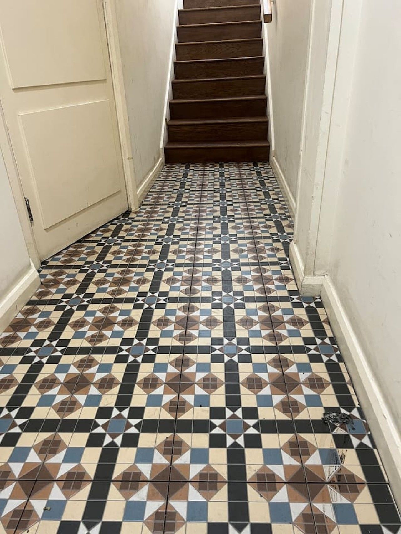 A hallway with a patterned tile floor and a wooden staircase.