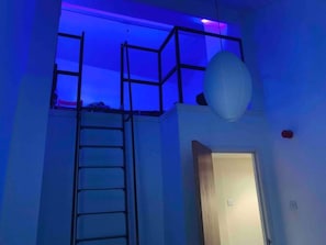 A room with a ladder leading to a mezzanine level, a door, and a hanging spherical light fixture. - Boss Places Mathew St 2 Bed duplex 2 bed sleeps 6 (Merseyside)