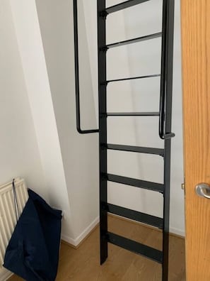 A metal ladder against a wall with a radiator and a blue bag on the floor. - Boss Places Mathew St 2 Bed duplex 2 bed sleeps 6 (Merseyside)