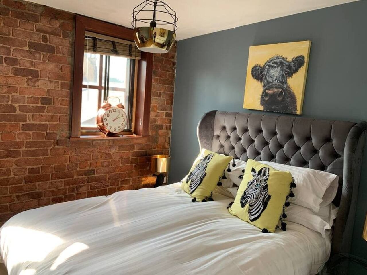 A bedroom with a brick wall, a tufted headboard, a bed with white linens, and two decorative pillows.