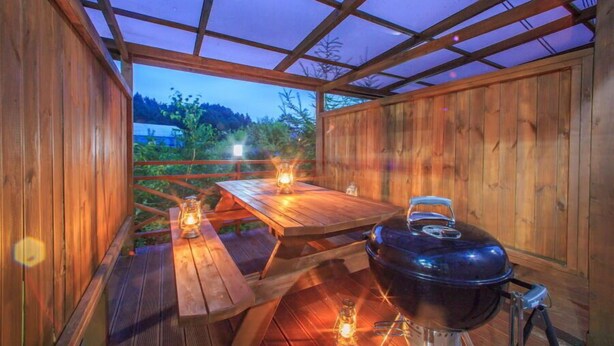 Una terraza de madera al aire libre con una parrilla y dos mesas, cada una con un farol.