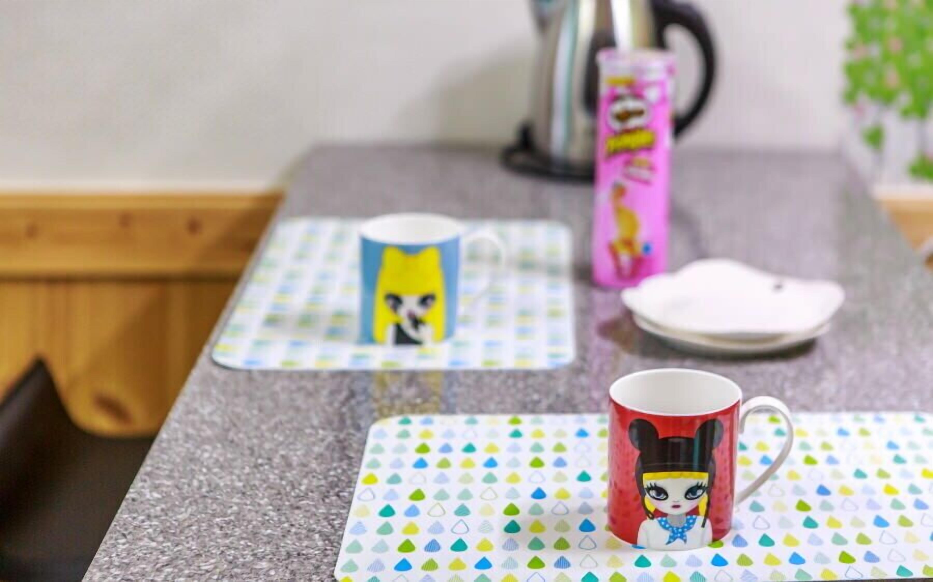 A kitchen counter with a coffee maker, a pink mug, and a red mug with a cartoon character.