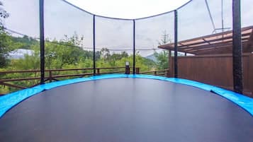 Un trampoline doté d’un filet de sécurité, entouré d’une terrasse en bois et offrant une vue sur la verdure.