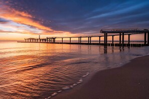 A pier extending into calm waters with a sunset sky.