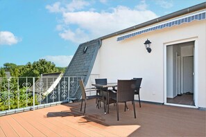 Eine Dachterrasse mit Tisch und Stühlen, einem Metallgeländer und einer Tür zu einem Innenbereich.