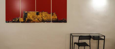 A room with a wooden floor, a black metal table with two chairs, and a large red and yellow painting on the wall.