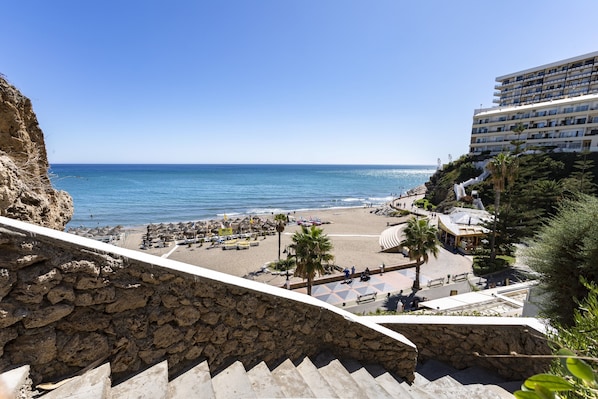 A coastal hotel with a beach view, stone steps leading to the beach, and a pool area.