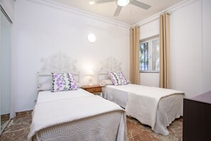 A bedroom with two beds, a nightstand, a ceiling fan, and a window with curtains.