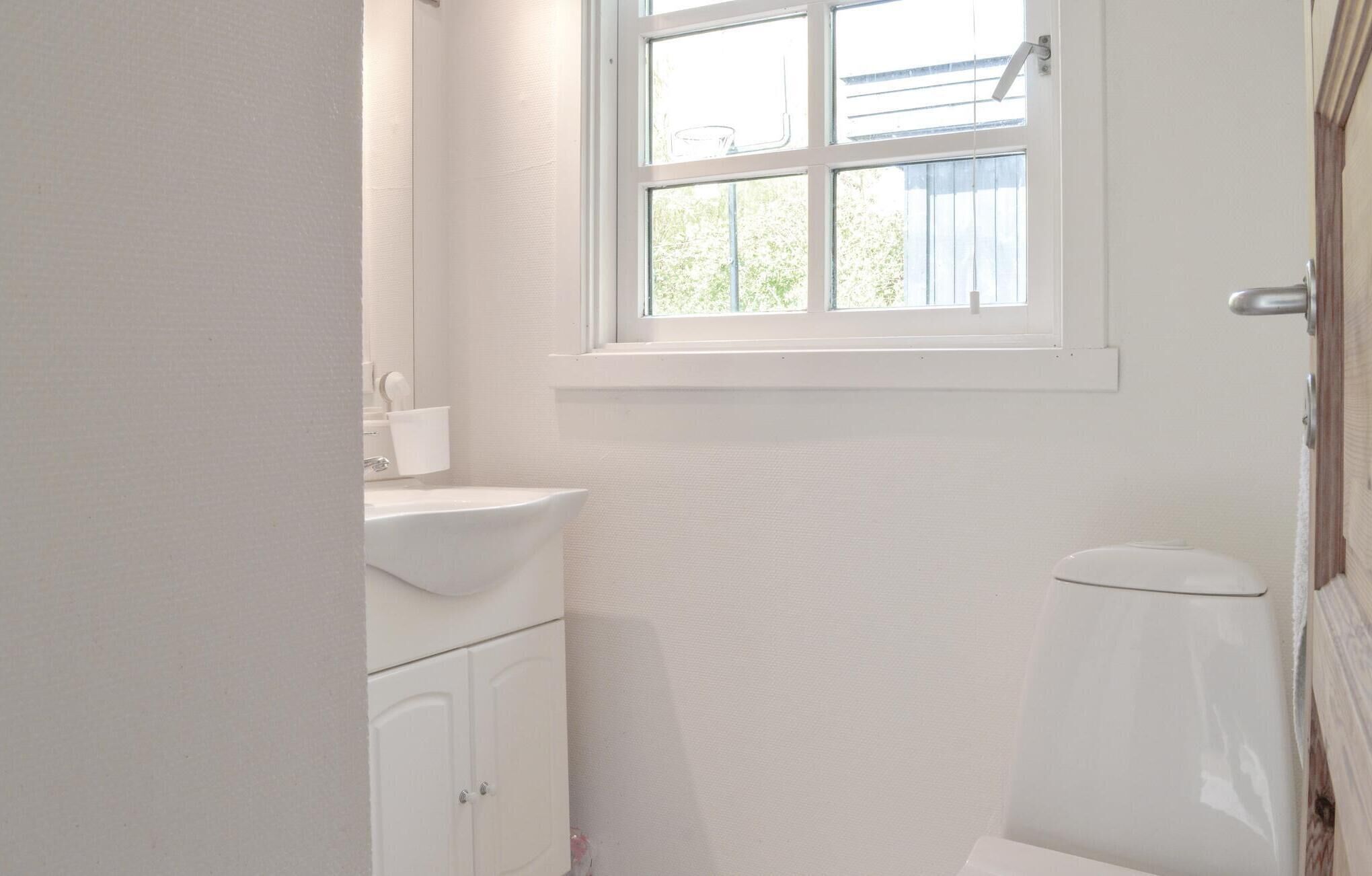 Un baño pequeño y blanco con ventana, lavamanos y retrete.