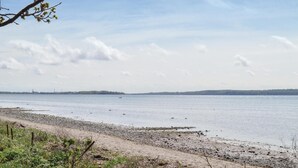 Une plage avec un ciel dégagé, une eau calme et une terre visible au loin.