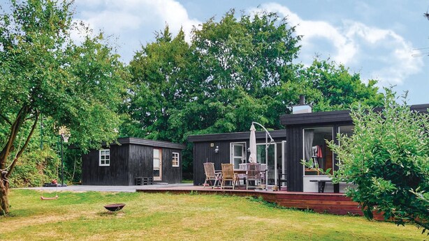 Une petite cabane en bois sombre, dotée d’un patio et entourée d’une végétation luxuriante.