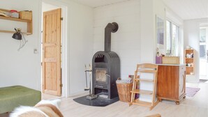 Un salon chaleureux avec un poêle à bois, un pouf vert, une chaise en bois et un panier en osier.