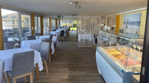 A restaurant with tables and chairs, a food display case, and large windows.