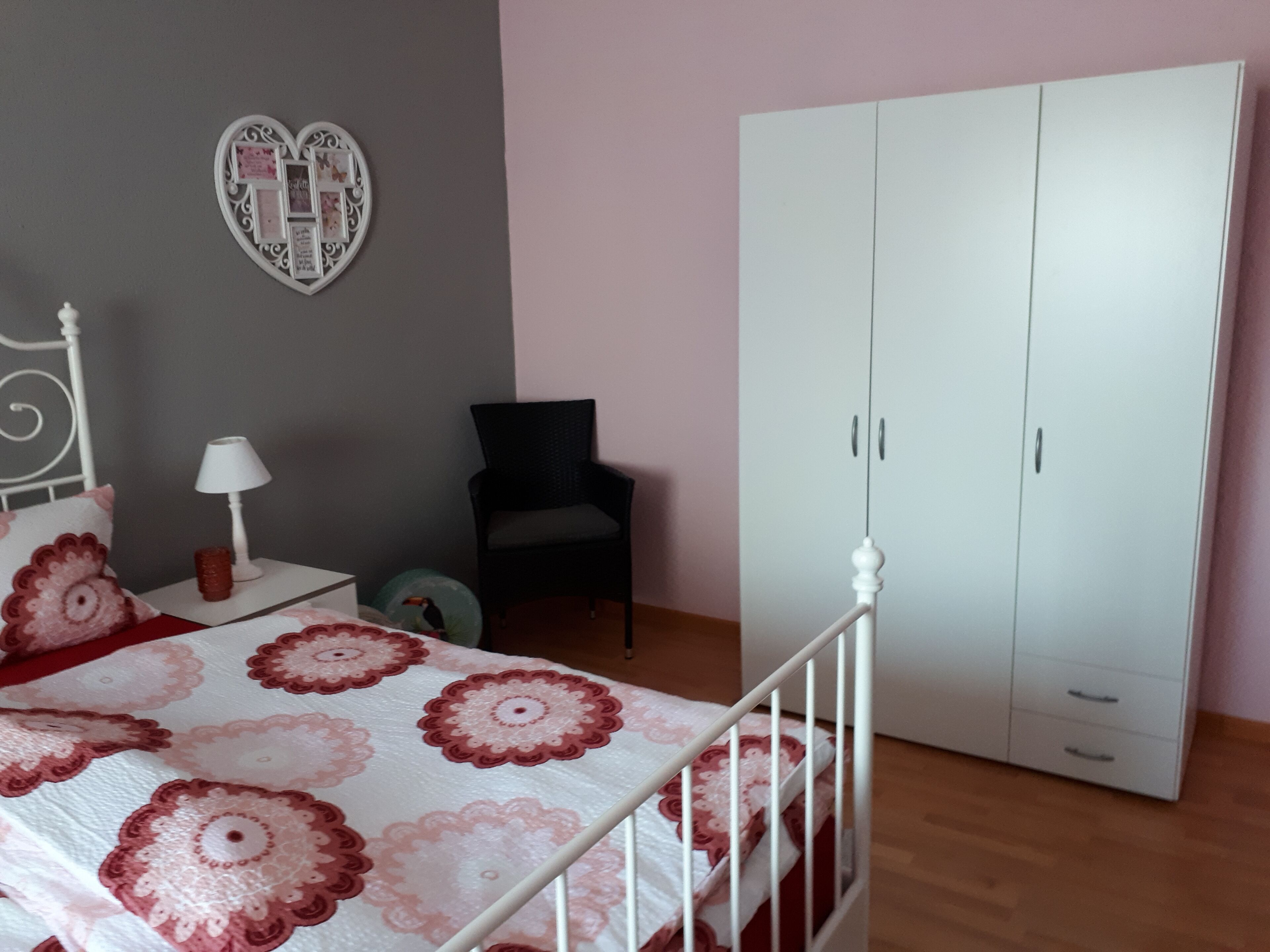 Un dormitorio con cama, armario, silla, lámpara y un adorno en la pared.