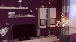 A living room with a flat-screen TV, wooden cabinets, a coffee table with magazines, and a decorative plant.