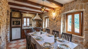 A rustic stone interior with a dining table set for four, a kitchen with a stove and oven, and a large window with a view. - Stunning home in Krivodol (Krivodol)