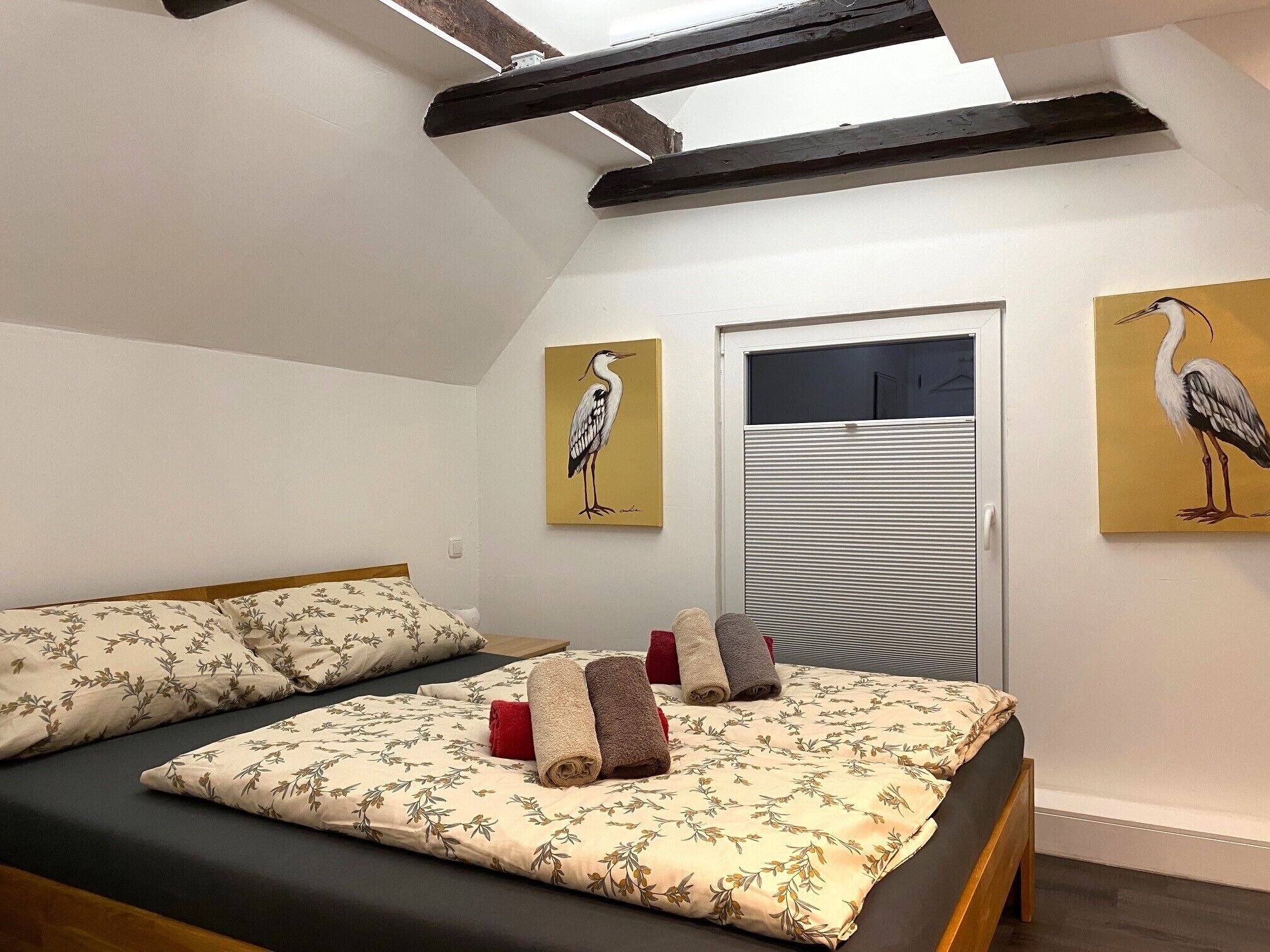 Un dormitorio con una cama, dos cuadros, una ventana y una puerta.