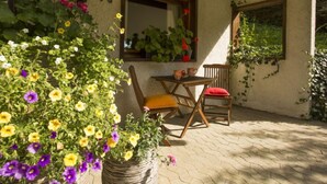 Een terras met een houten tafel en stoelen, omgeven door bloemen en planten in potten.