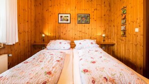 Een kamer met houten lambrisering en twee bedden, elk met bloemenbeddengoed en bedlampjes.